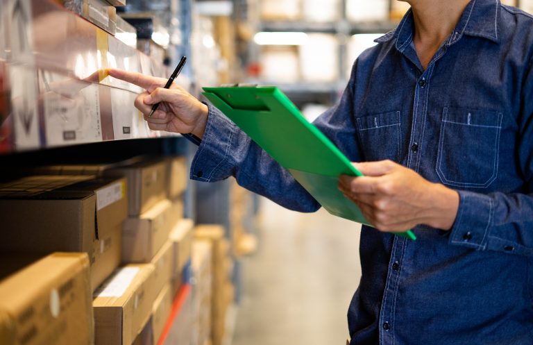 Manager man worker doing stocktaking of product management in cardboard box on shelves in warehouse. Physical inventory count.